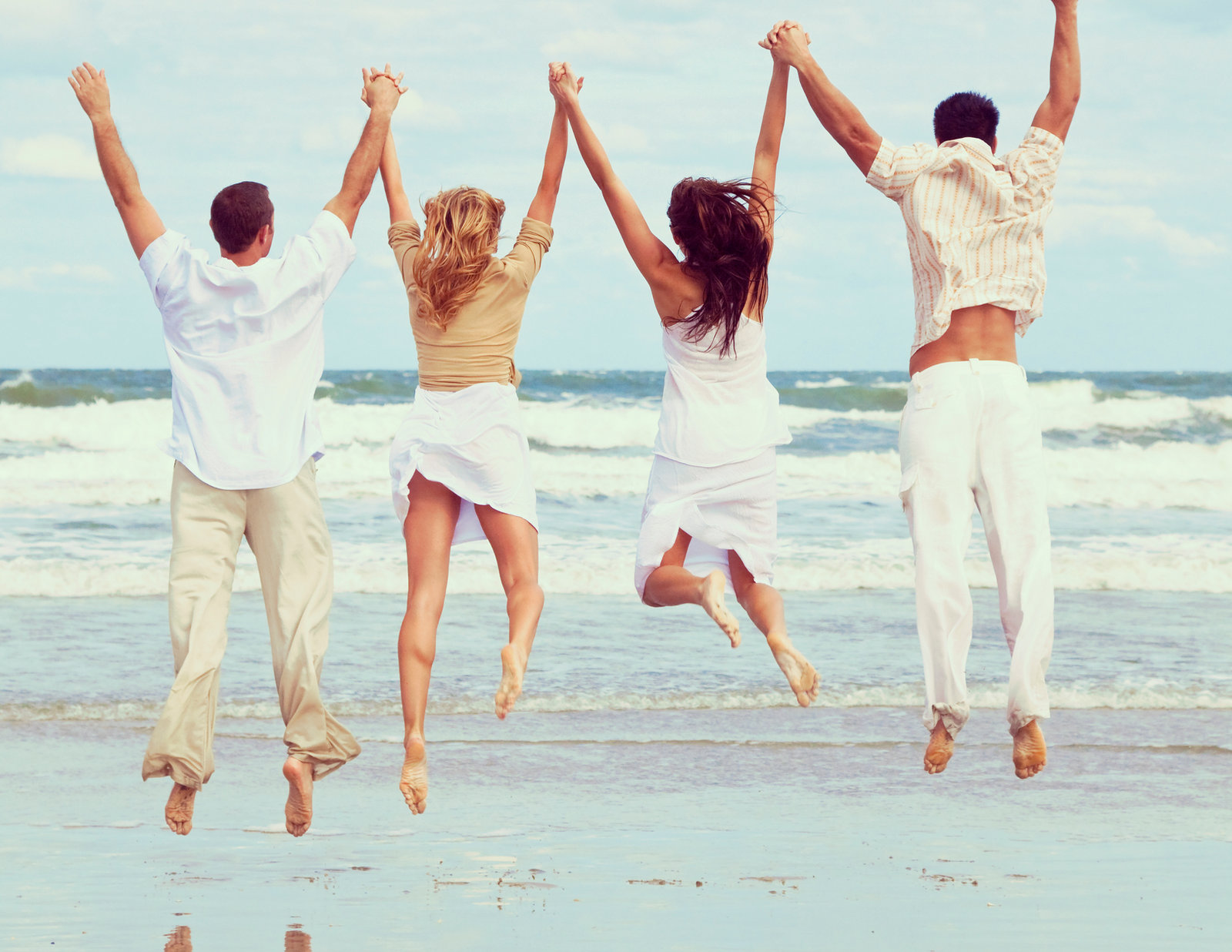 4 people leaping on beach holding hands
